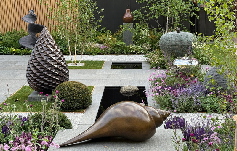 James Parker Sculpture trade stand on Main Avenue at RHS Chelsea Flower Show, featuring bronze pine cone and DNA of a Dancer slate sculpture.