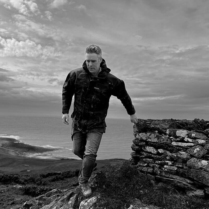 James Parker beside a stone cairn at Knock Farm, Galloway, overlooking the sea.