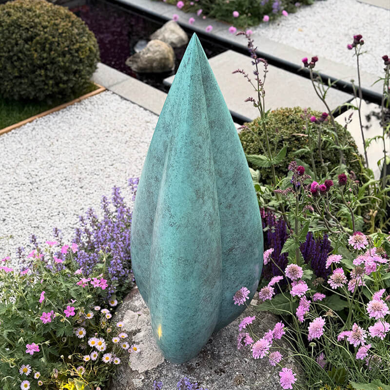Limited edition bronze Bud sculpture by James Parker with white-green patina installed in a garden setting