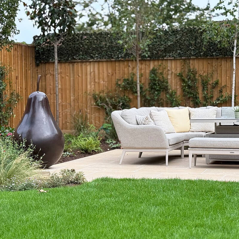 Limited edition bronze pear sculpture by James Parker placed beside a terrace in a landscaped Berkshire garden