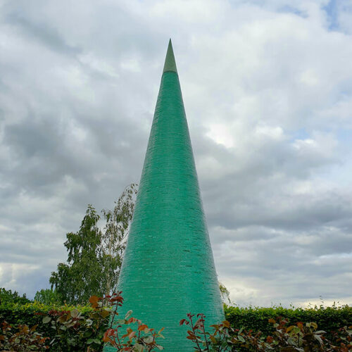 Monumental stacked glass Cone sculpture by James Parker with bronze finial, showing green light refraction through layered glass against the sky.