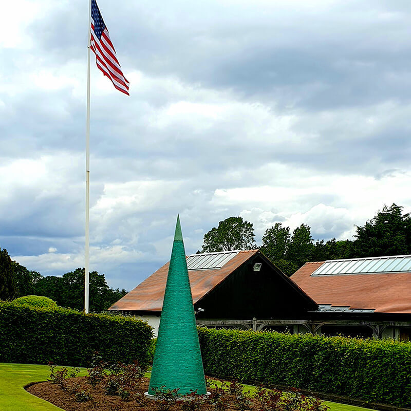 Upward view of James Parker’s monumental stacked glass Cone sculpture, focusing on the bronze vertex and layered glass refracting green light.