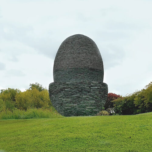 Monumental slate acorn sculpture by James Parker, constructed in layered stone and installed as a focal point within a landscaped garden.