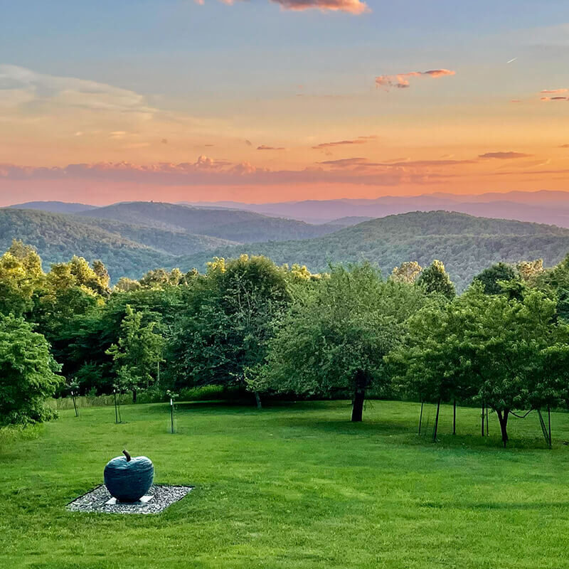 Contemporary stone apple sculpture by James Parker positioned within an open lawn landscape at sunset.
