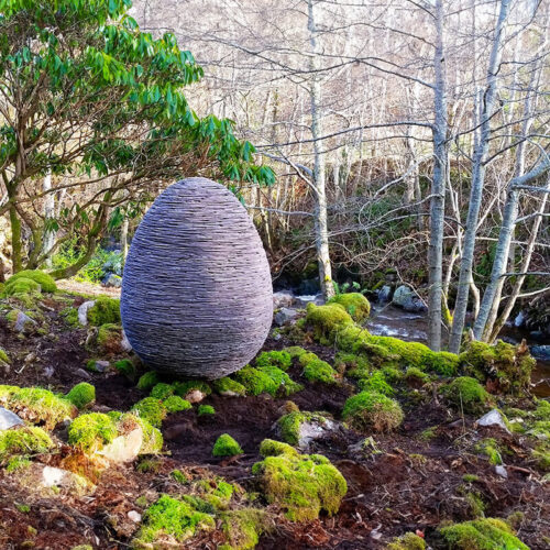 Contemporary stacked slate egg sculpture “Creation” by James Parker installed in a garden setting.