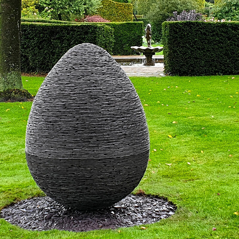 Stacked slate egg sculpture by James Parker crafted from Penrhyn Welsh slate, installed in a private garden.