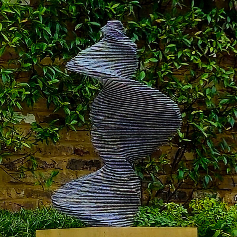 DNA of a Dancer stacked slate spiral sculpture by James Parker installed in a landscaped garden setting.