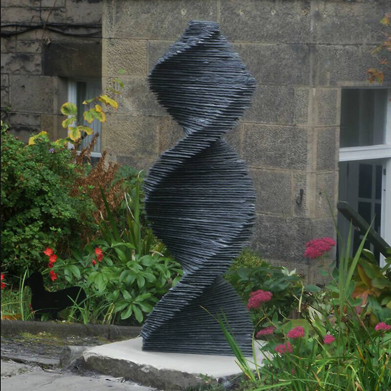 Stacked slate spiral sculpture “Garrochar Twist” by James Parker installed as a garden centrepiece on a sandstone base.