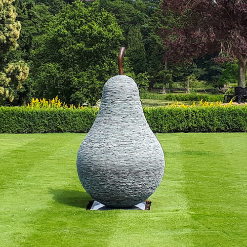 Large stacked slate pear sculpture with bronze stem by James Parker set within a landscaped formal garden.