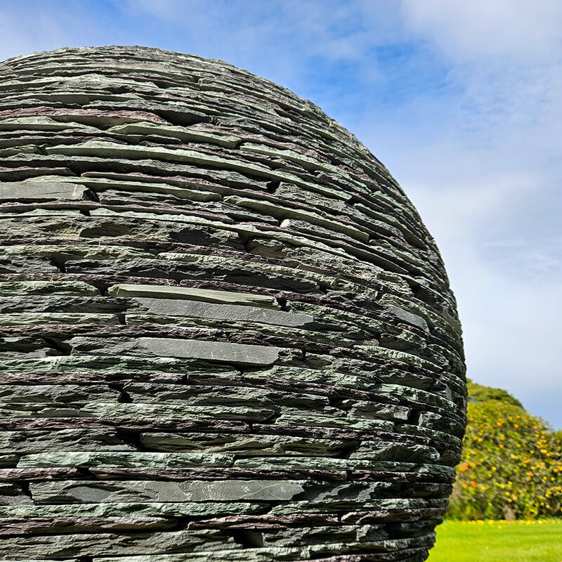 Large stacked slate sphere sculpture by James Parker installed as a contemporary garden focal point.