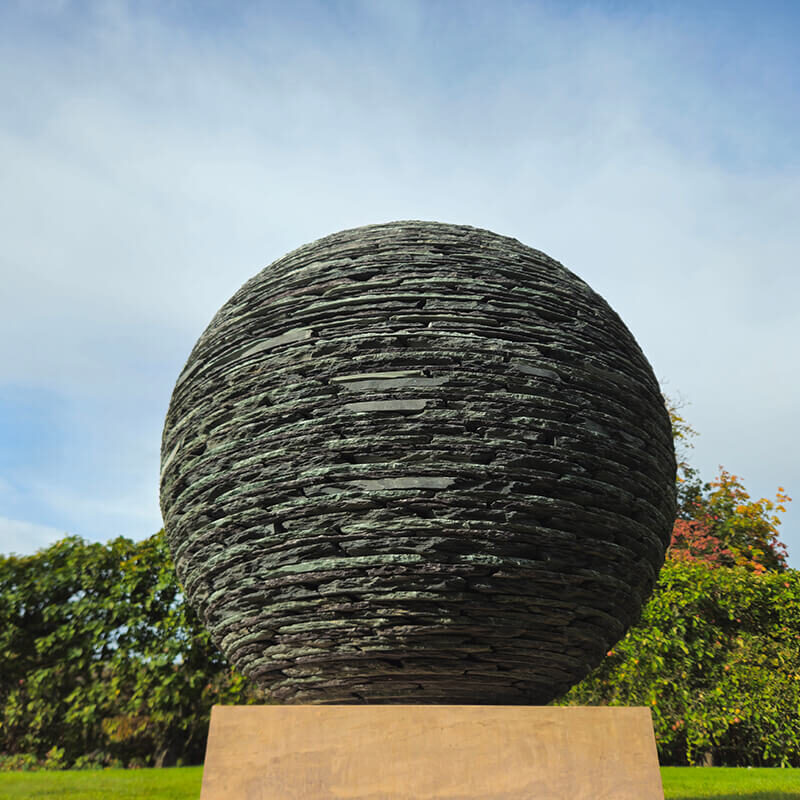 Stacked stone sphere sculpture by James Parker installed on a Corsehill sandstone plinth in a garden setting.