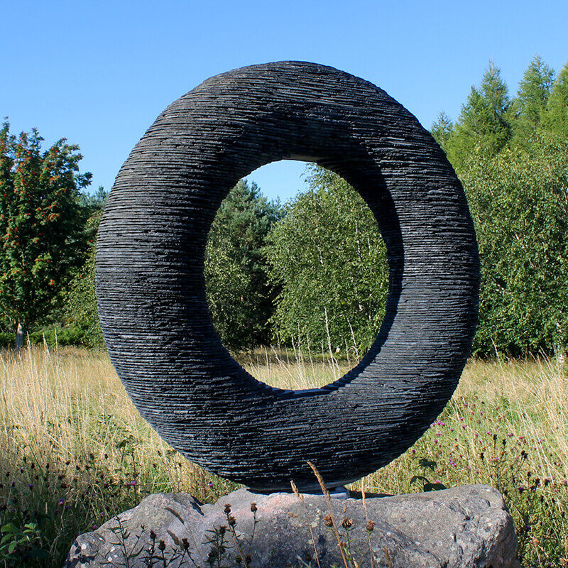 Abstract stacked slate torus sculpture titled Spirit by James Parker installed in an open landscape.
