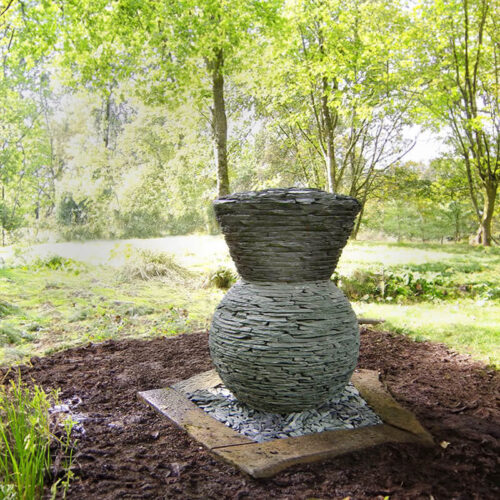 Stacked slate thistle sculpture by James Parker installed in a woodland garden setting.