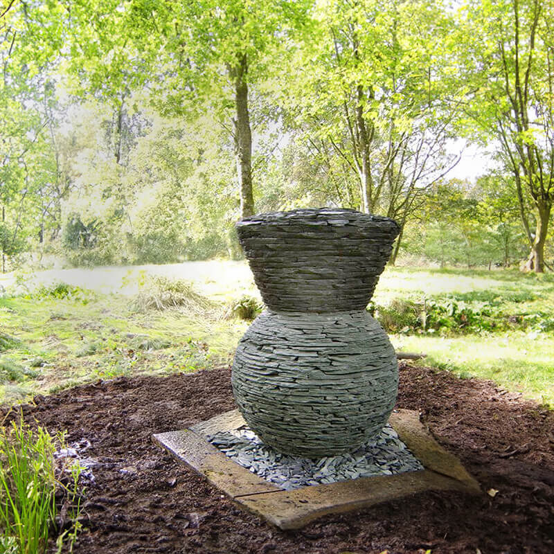 Stacked slate thistle sculpture by James Parker installed in a woodland garden setting.