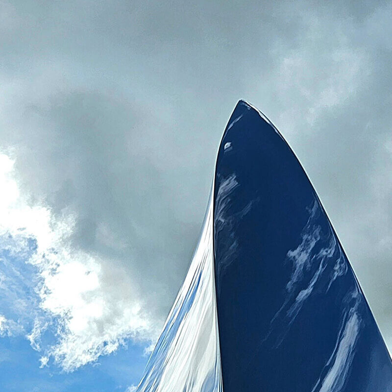 Detail of mirror-polished stainless steel Leaf sculpture by James Parker reflecting clouds as it leaves the workshop.