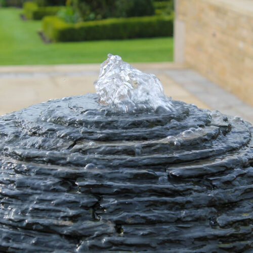Detail of a slate sphere water sculpture by James Parker showing water emerging across layered Lakeland Blue slate.