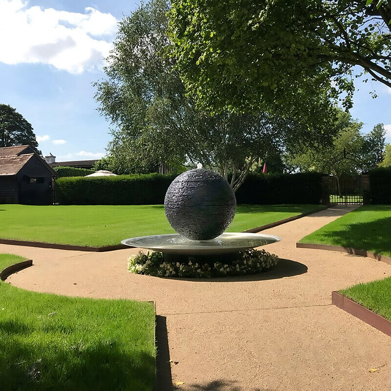 Bespoke slate sphere water sculpture by James Parker serving as a contemporary garden centrepiece in Cambridgeshire.