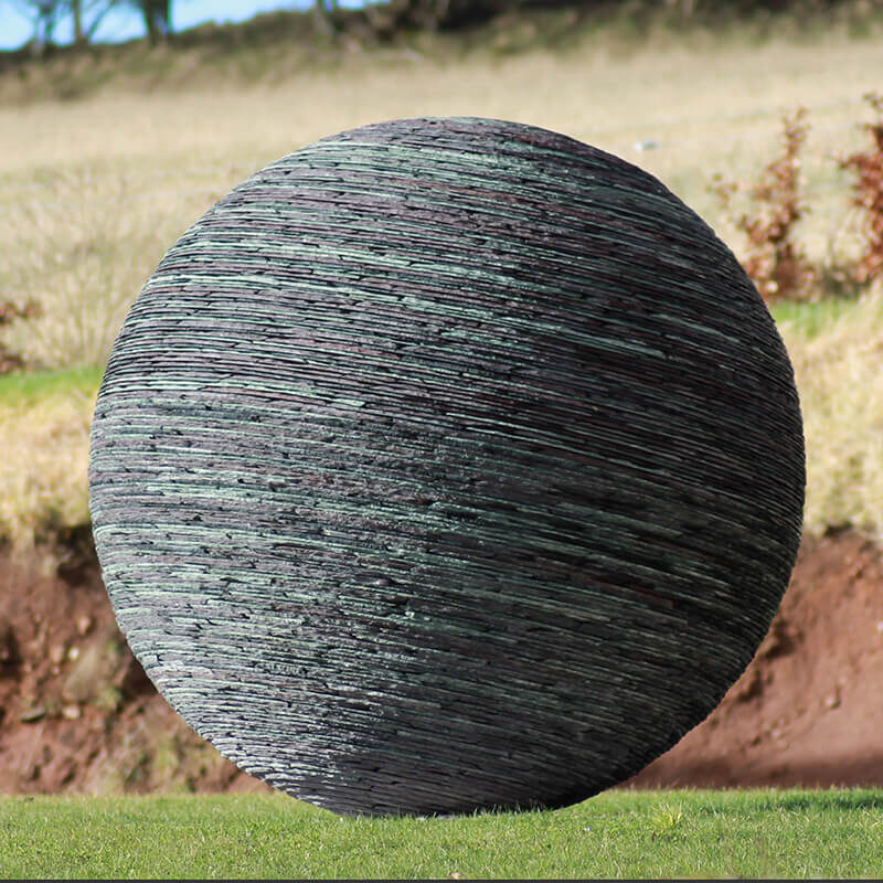 Large stacked slate sphere sculpture by James Parker installed within an open landscape setting.