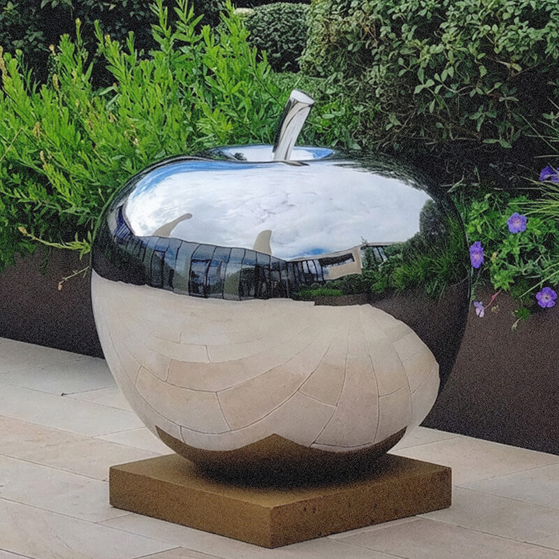 Mirror-polished stainless steel Apple sculpture installed on a contemporary rooftop terrace, reflecting surrounding architecture.