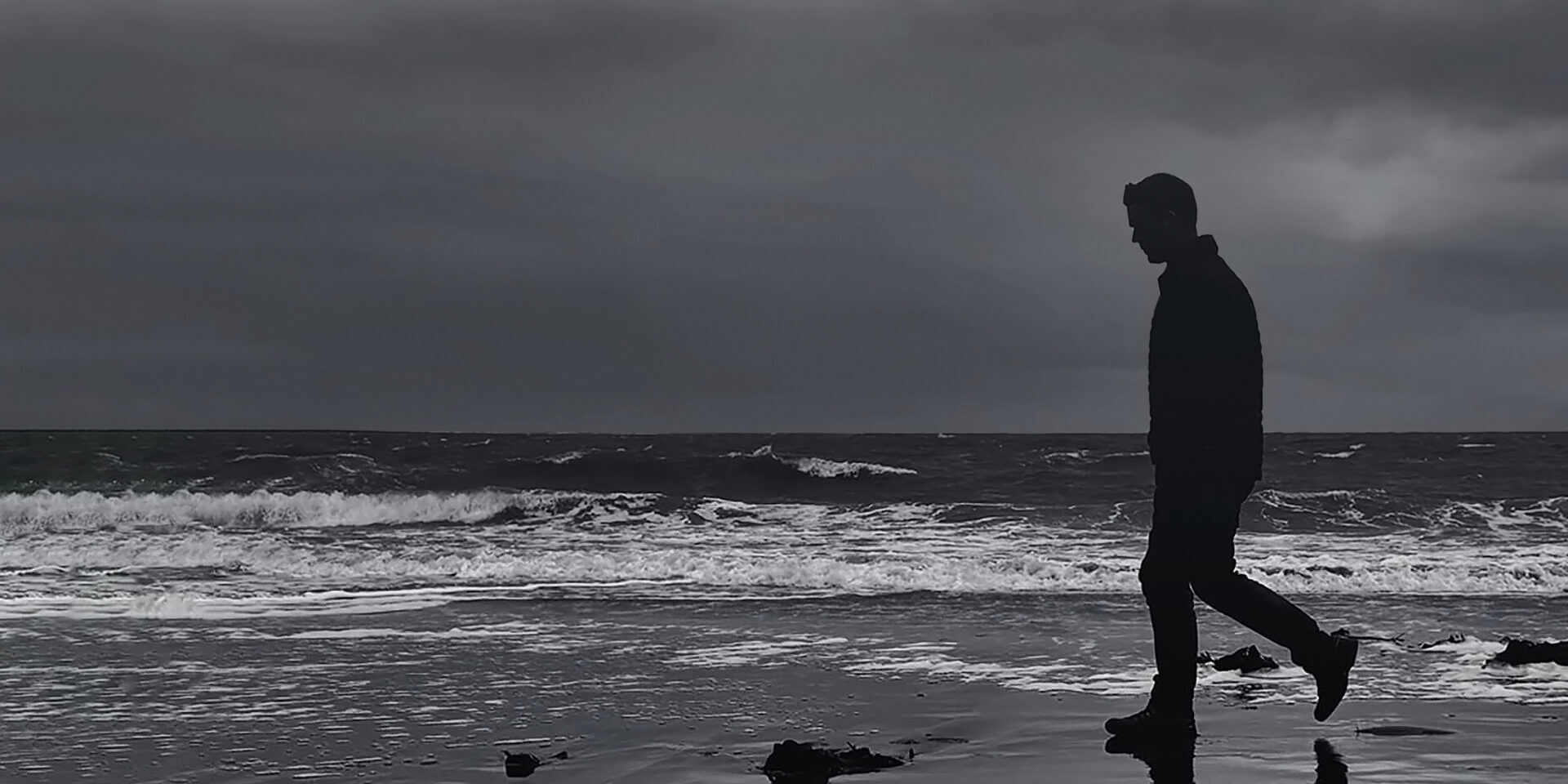 James Parker silhouetted walking along a Galloway beach in southwest Scotland, waves behind and reflection on wet sand.