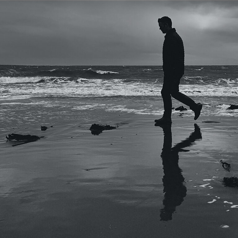 James Parker silhouetted walking along a Galloway beach in southwest Scotland, waves behind and reflection on wet sand.