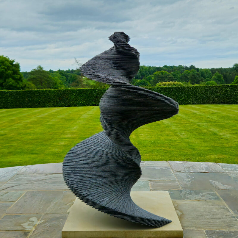 Slate spiral sculpture in the form of a helix in a beautiful garden setting.